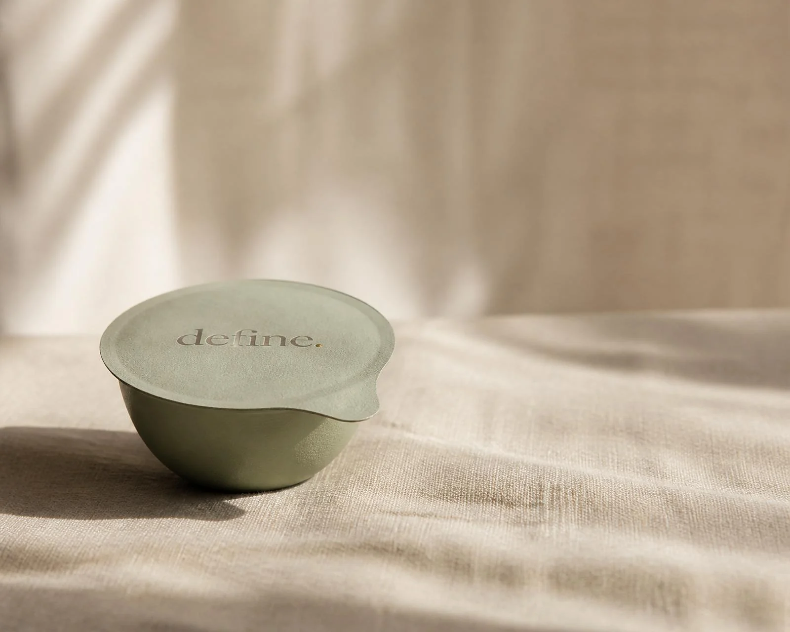 A sage-green define. nutrition pod, sealed with the define. lid, resting on soft linen in morning light.